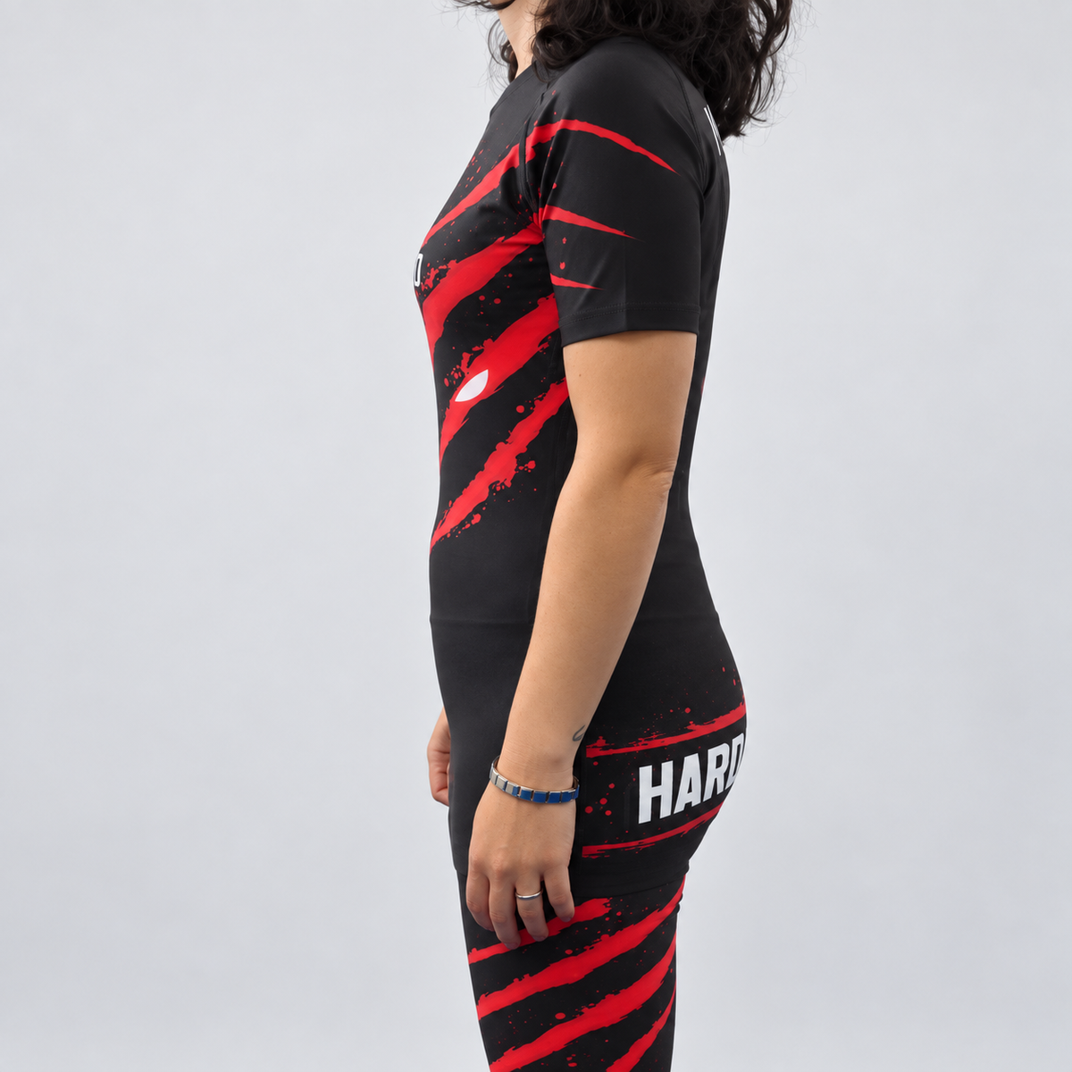 Rashguard Hard to Handle de mulher, de manga curta, preta e vermelha, vestida por modelo, vista lateral esquerda com detalhes vermelhos na manga.